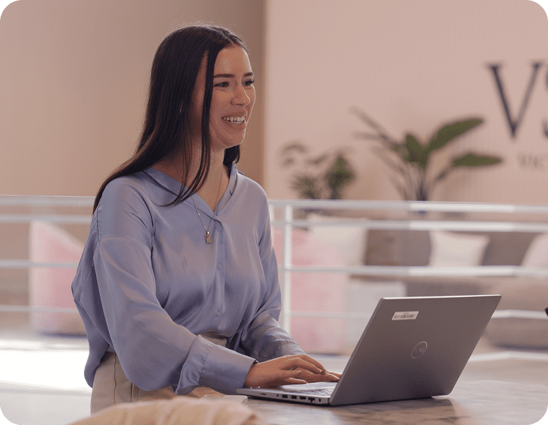 Rectangle 36 A smiling woman working at a laptop computer in a modern office setting